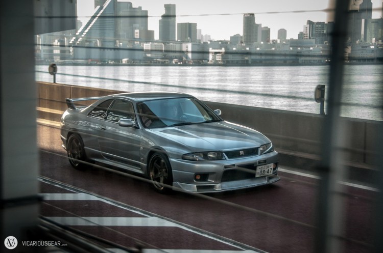 A clean Skyline R33 with lip and Nismo rims crossing the rainbow bridge in Tokyo.