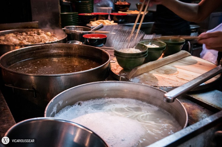 Huge stock pots with (from front to back) noodles, broth and possibly the signature hot sauce being made.